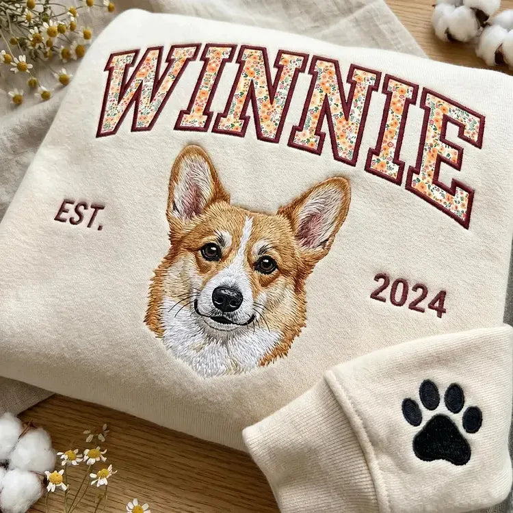 Cream sweatshirt with WINNIE in floral letters above an embroidered corgi, with a paw print on the cuff