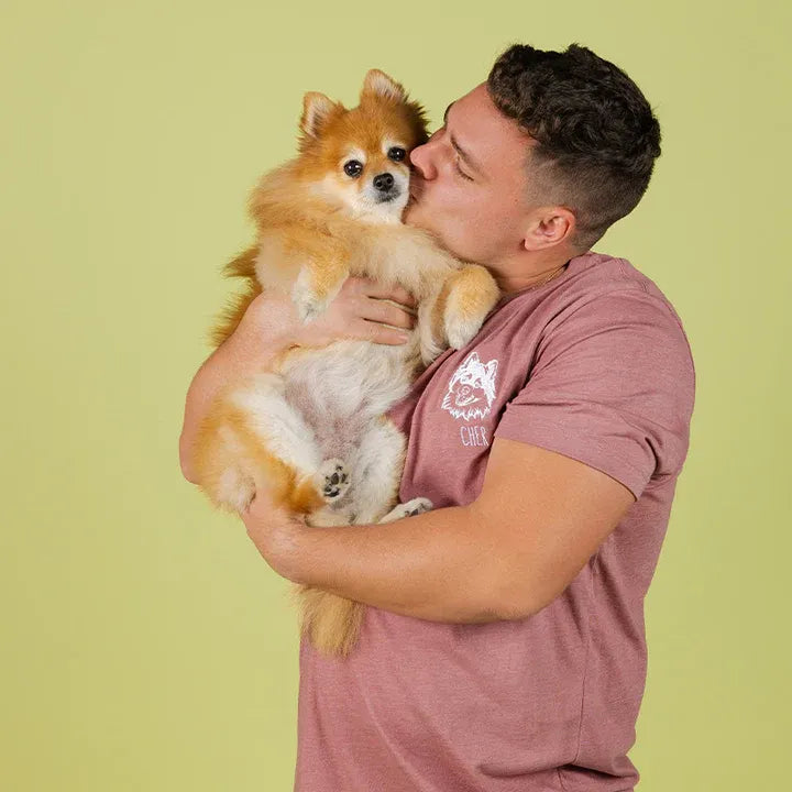 Man kissing his Pomeranian, wearing a mauve tee with the dog's white line art portrait
