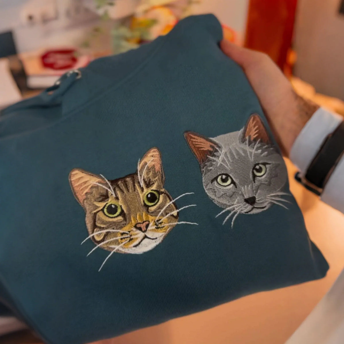 Tabby and gray cat portraits embroidered together on a teal sweatshirt