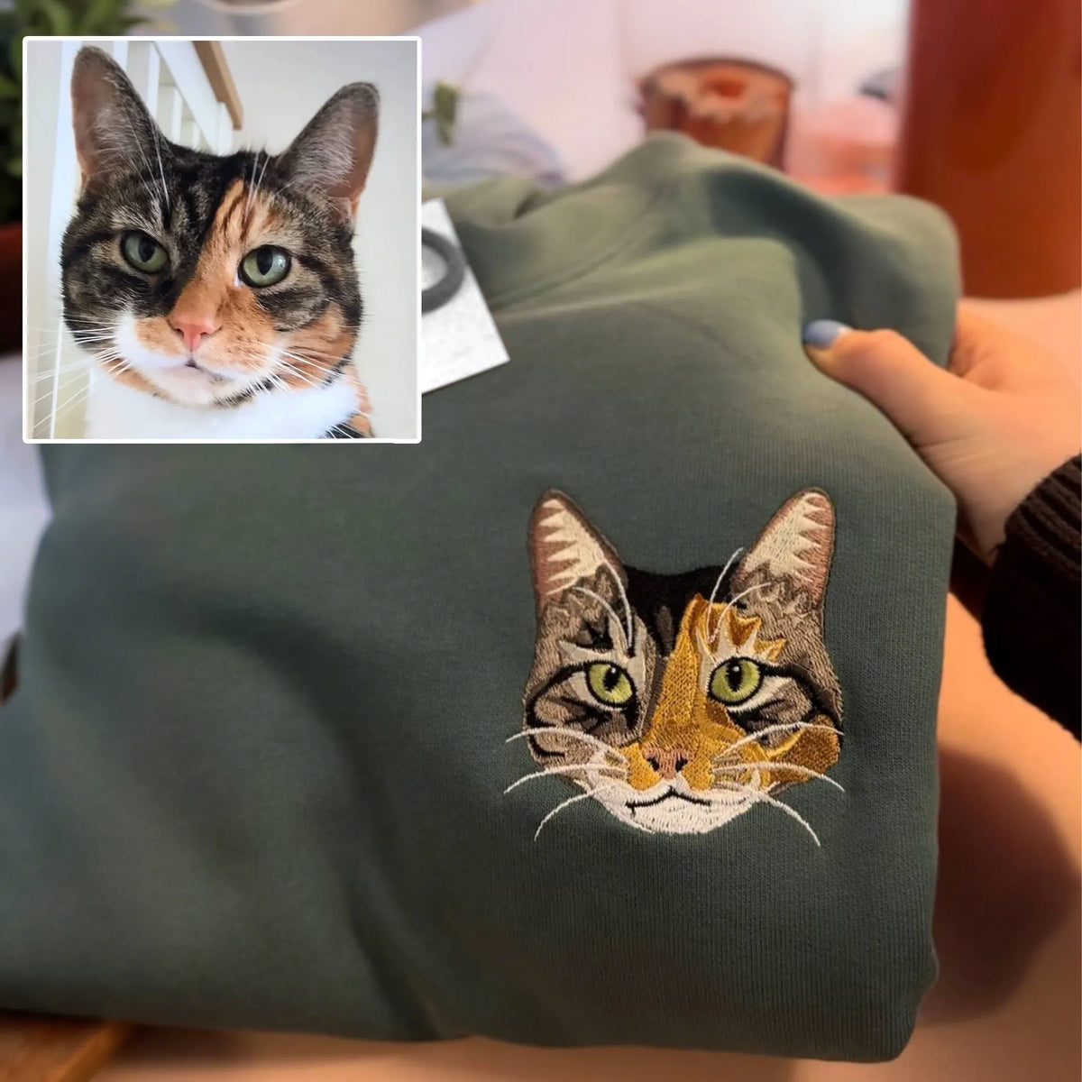 Calico cat face embroidered in full color on a dark green sweatshirt
