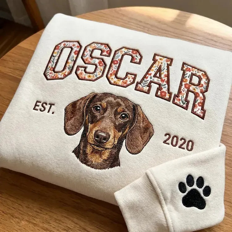 Cream sweatshirt with OSCAR in floral appliqué letters, an embroidered dachshund and a paw on the cuff