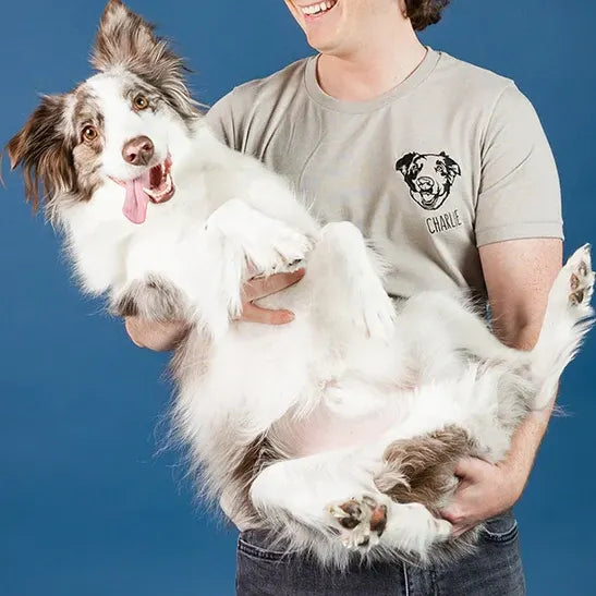 Person holding a border collie while wearing a tan tee with the dog's line art portrait and name Charlie