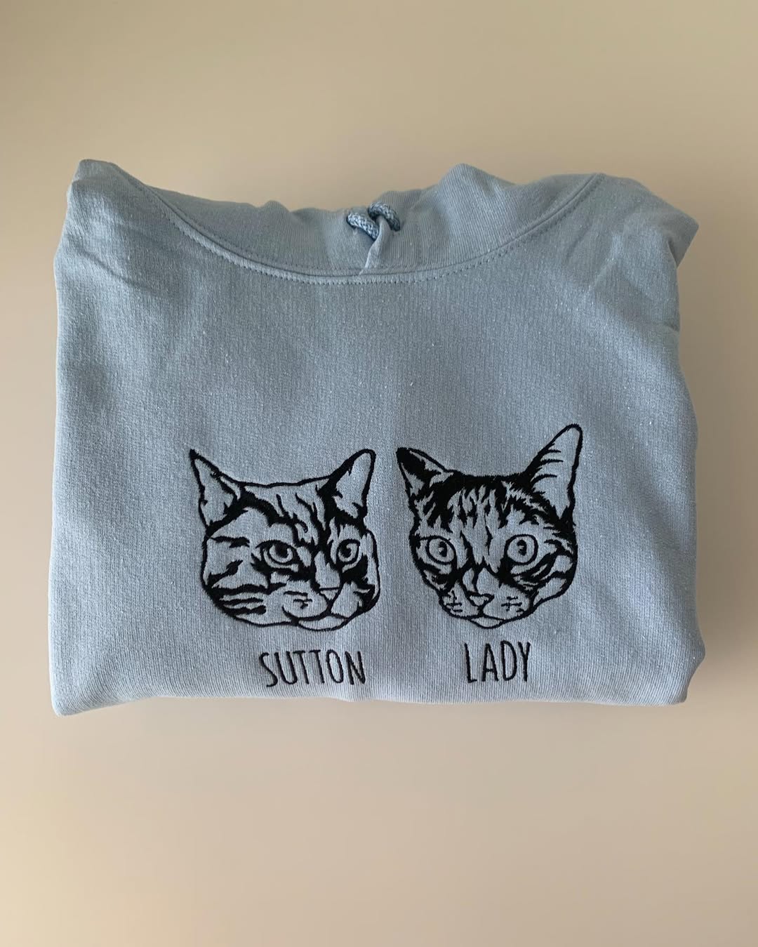 Two cat outline portraits named Sutton and Lady embroidered side by side on a gray hoodie