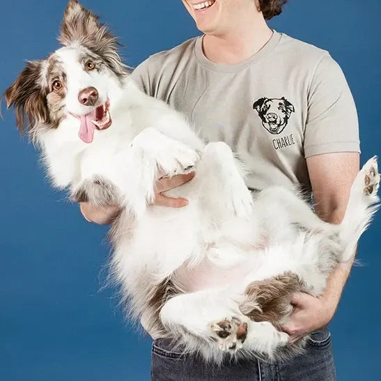 Man holding a border collie, wearing a tan tee with the dog's line art portrait and the name Charlie on the chest