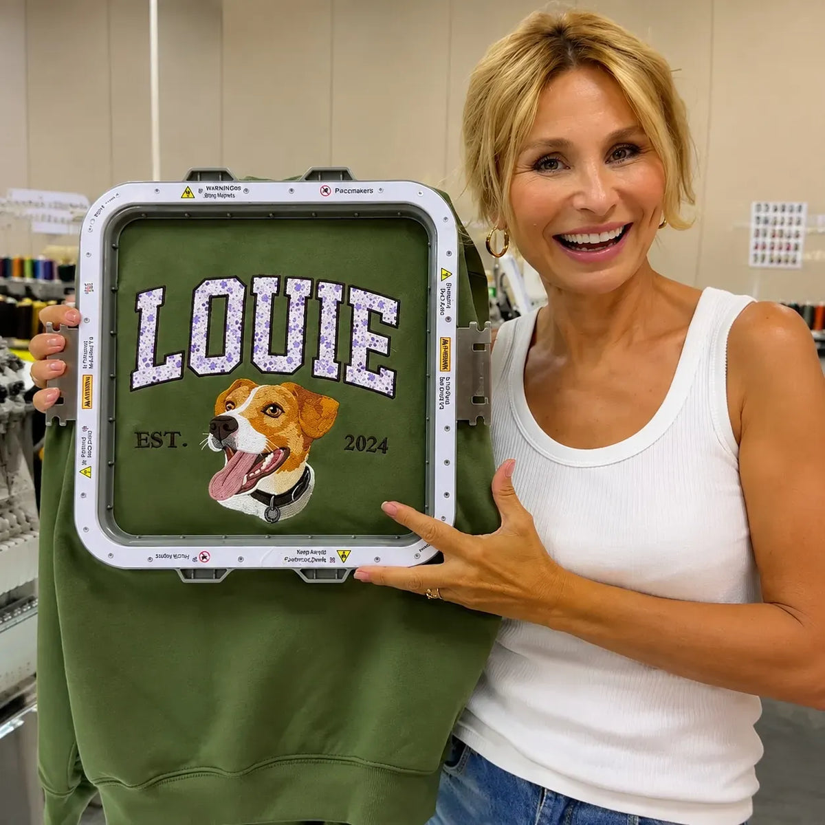 Smiling woman holding a green sweatshirt in an embroidery hoop with LOUIE and a beagle portrait