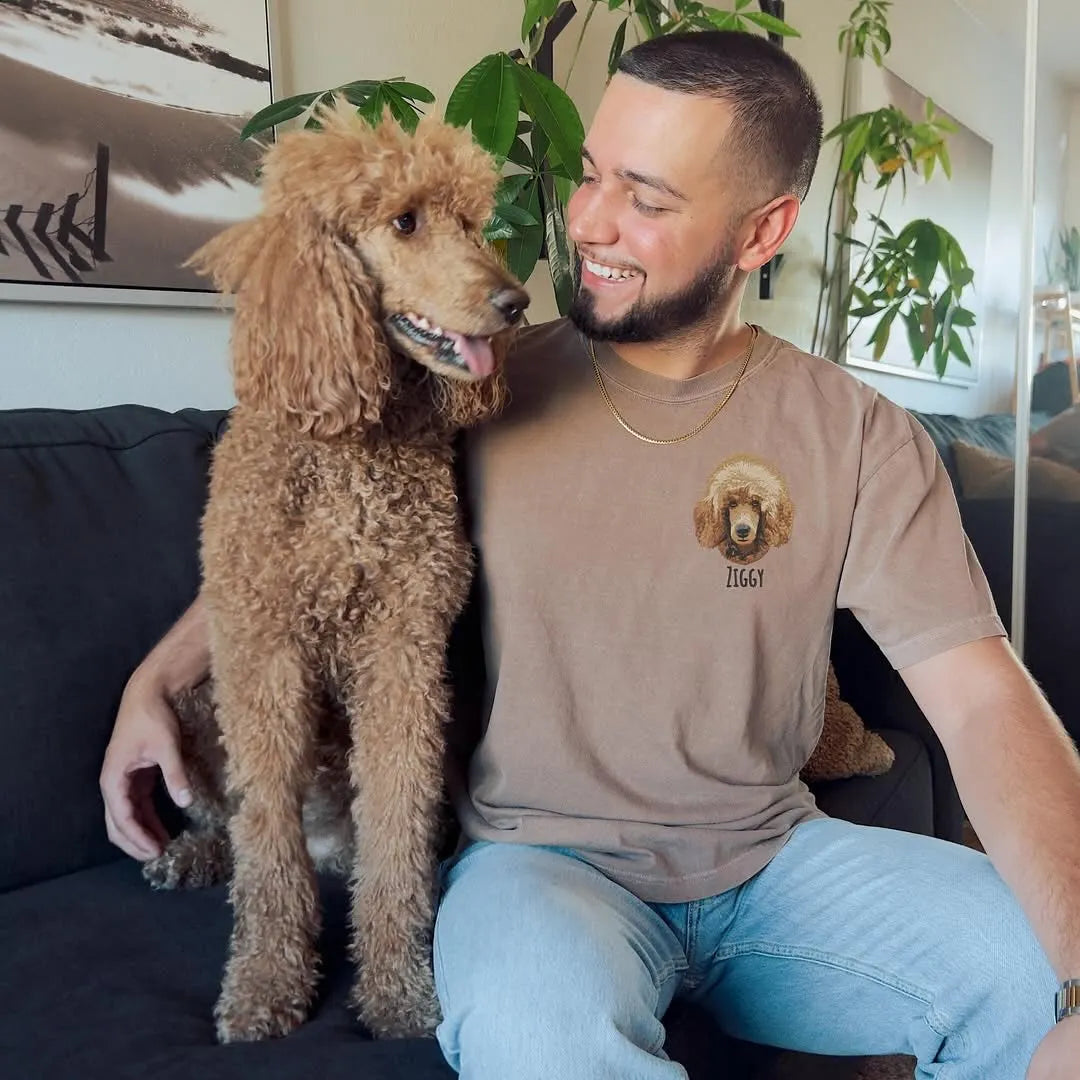 Man hugging his standard poodle while wearing a tan tee with the poodle's embroidered portrait on the chest