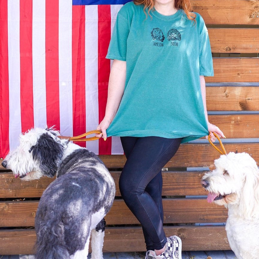 Woman in a teal tee embroidered with two dog outlines, walking her sheepdog and doodle