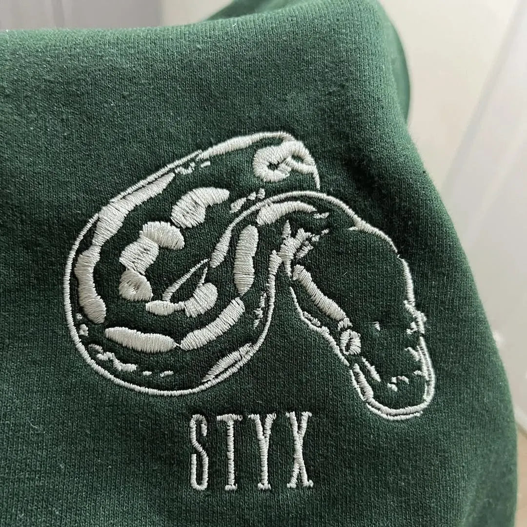 Forest green sweatshirt with a white outline ball python embroidery and the name STYX