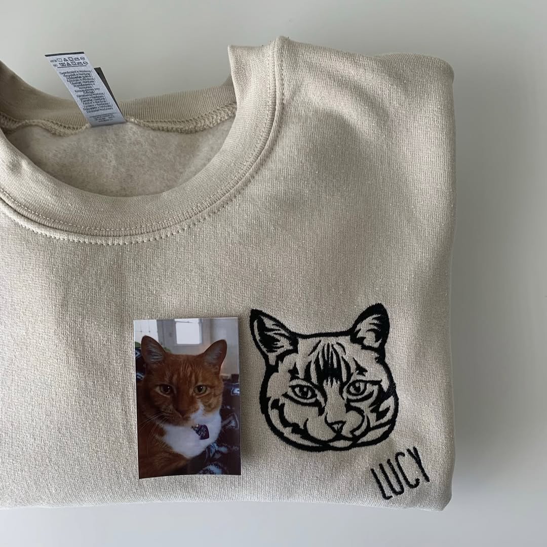 Cream sweatshirt with a line art cat portrait and the name Lucy, shown with the cat's photo