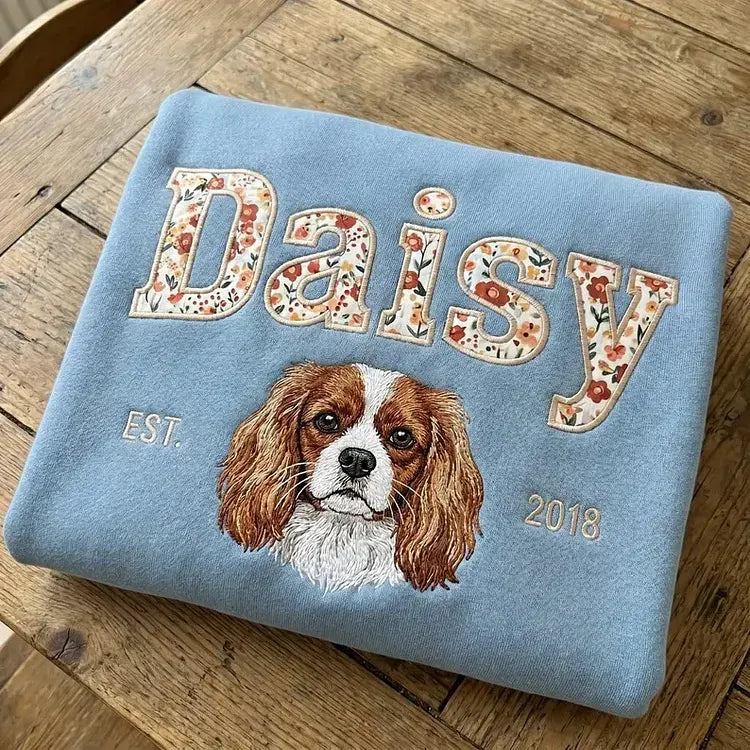 Light blue sweatshirt with Daisy in floral appliqué letters above an embroidered Cavalier King Charles spaniel