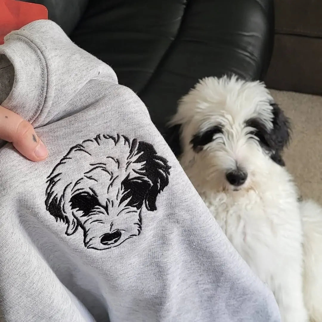 Gray sweatshirt with a black outline sheepadoodle portrait, held next to the fluffy black and white dog