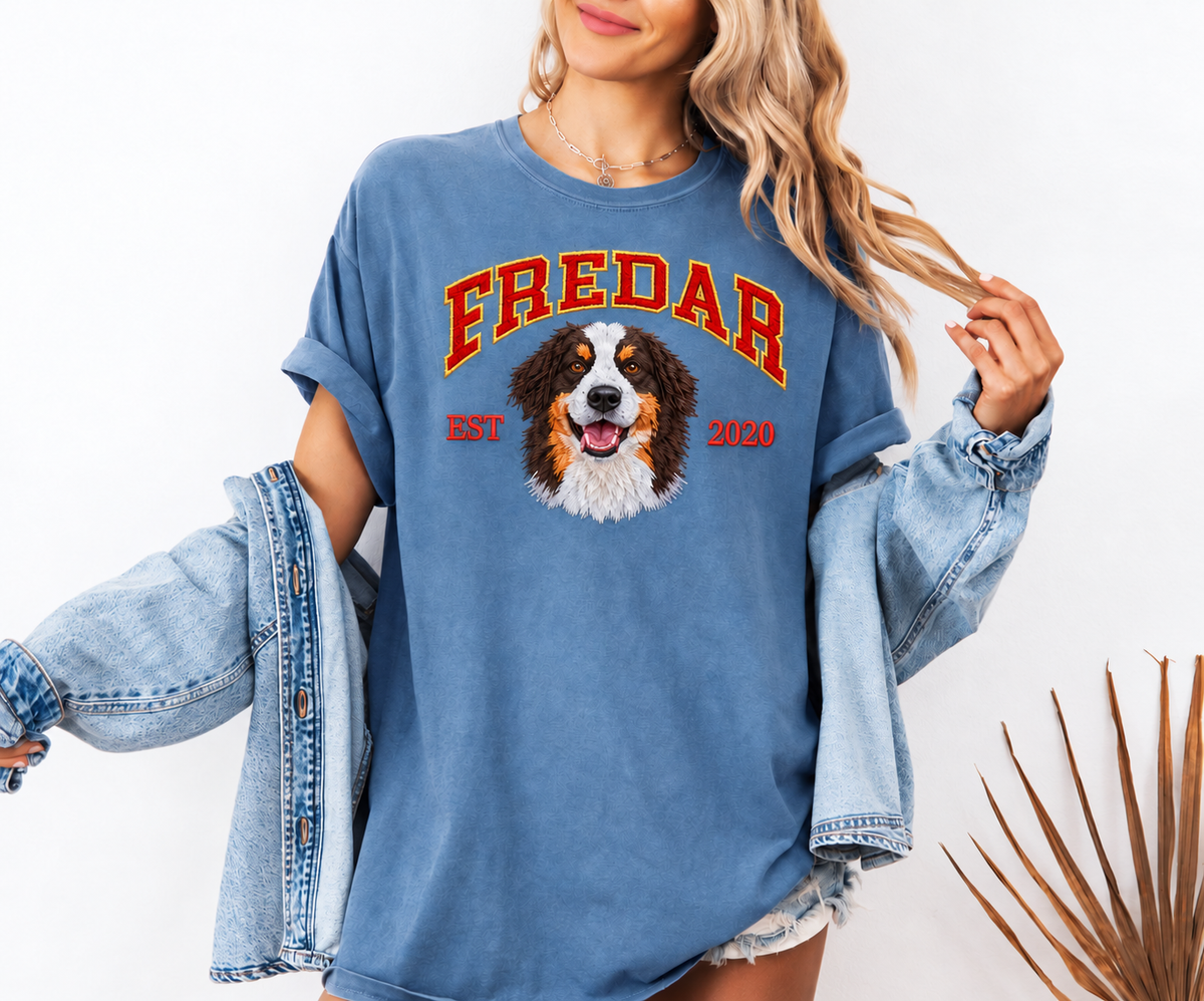 Woman wearing a blue washed T-shirt with red and gold FREDAR lettering, an embroidered dog portrait and EST 2020, with a denim jacket draped over her arms