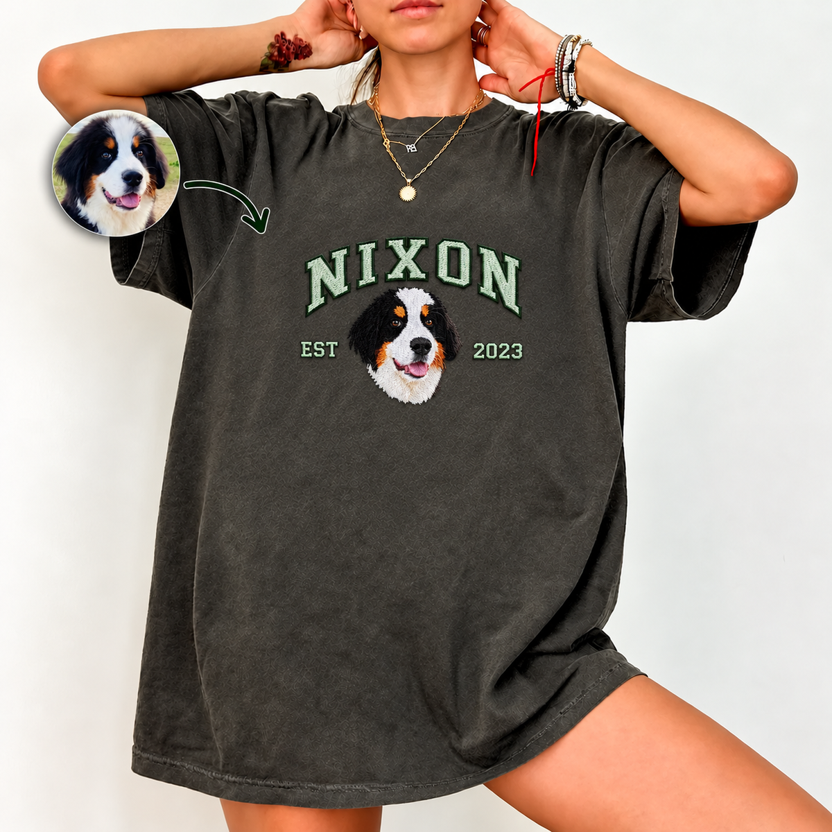 Woman wearing a charcoal washed T-shirt with NIXON lettering, a small embroidered Bernese mountain dog portrait, EST 2023, and a circular original dog photo inset