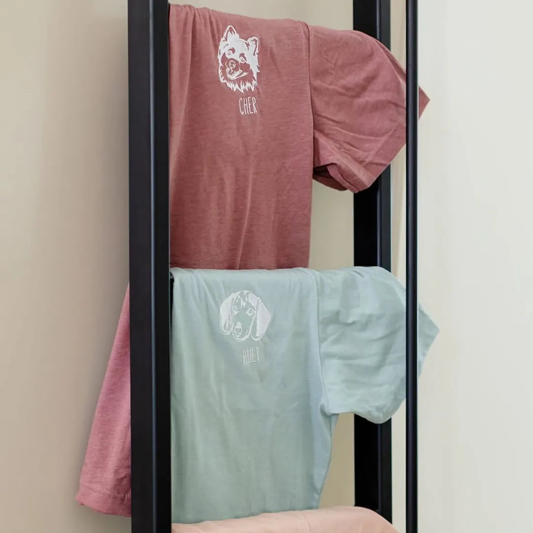 Mauve and mint tees with white embroidered pet line art hanging on a rack