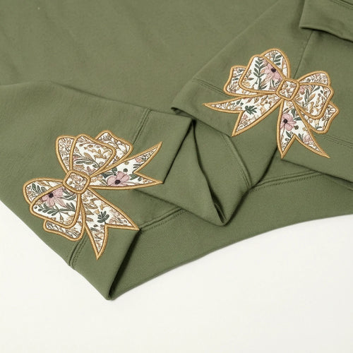 Close-up of cream floral bow appliqués on the cuffs of an olive sweatshirt