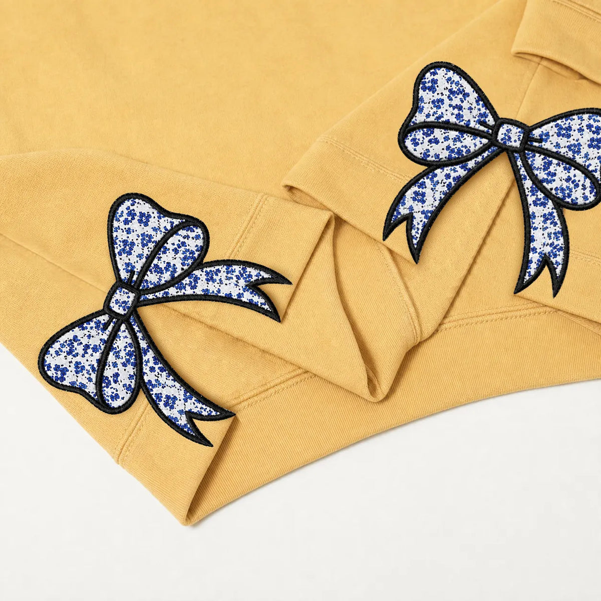 Close-up of blue floral bow appliqués on a mustard sweatshirt