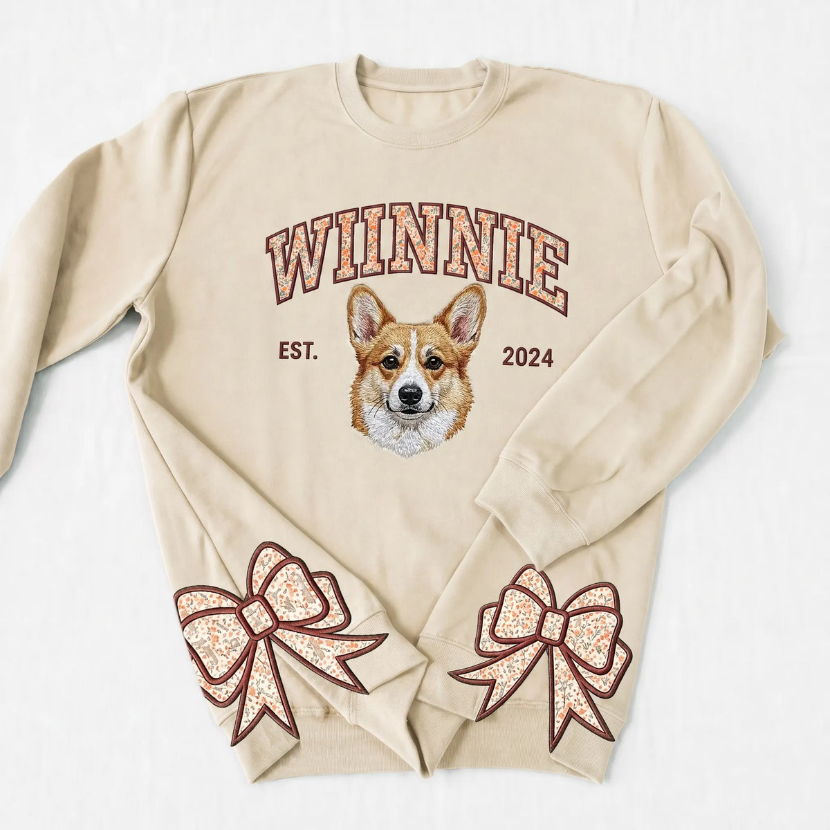 Sand sweatshirt with WINNIE in floral letters above an embroidered corgi and floral bows on the cuffs