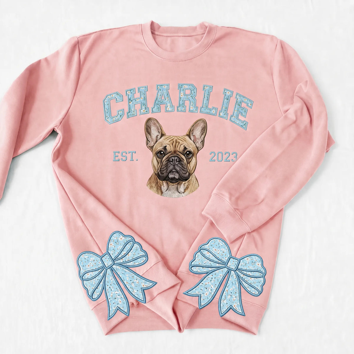 Pink sweatshirt with CHARLIE in light blue floral letters above an embroidered French bulldog and blue bows on the cuffs
