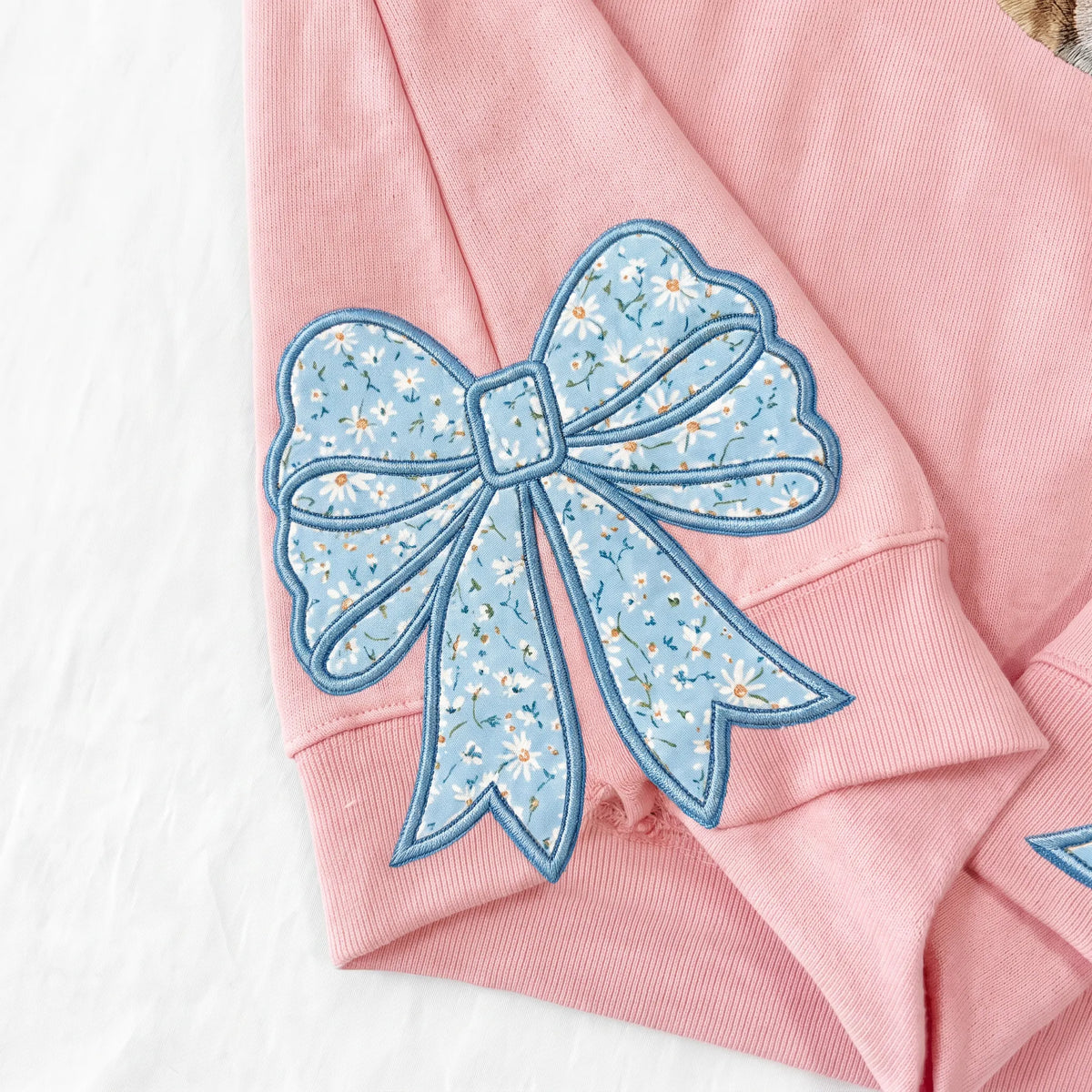 Close-up of a light blue floral bow appliqué on a pink sweatshirt cuff