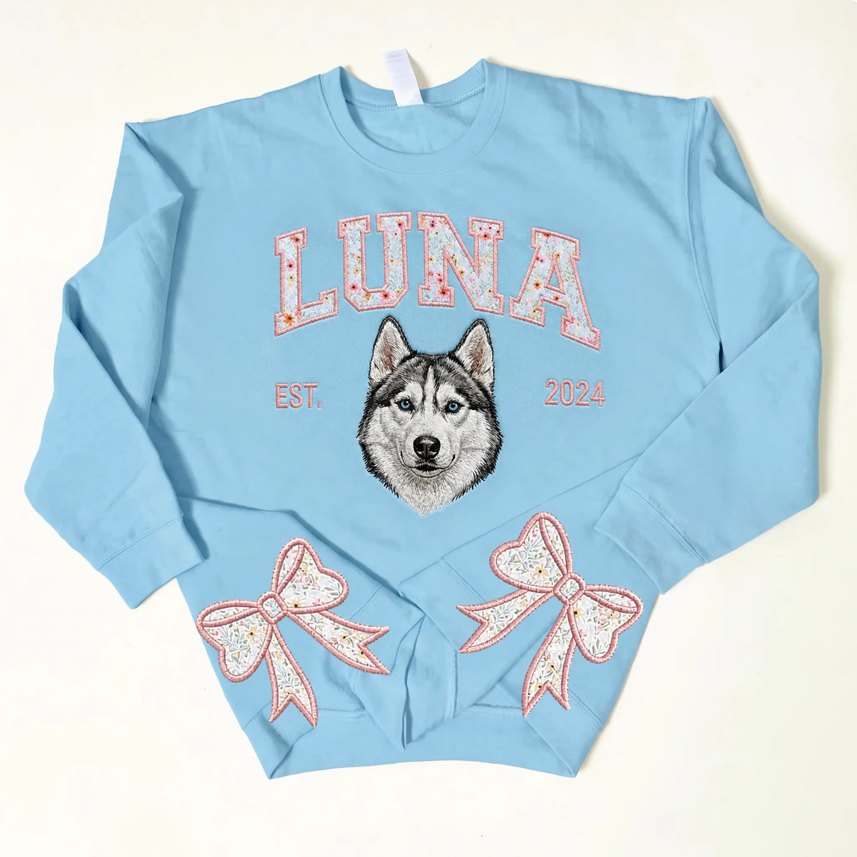 Light blue sweatshirt with LUNA in pink floral letters above an embroidered husky and pink bows on the cuffs