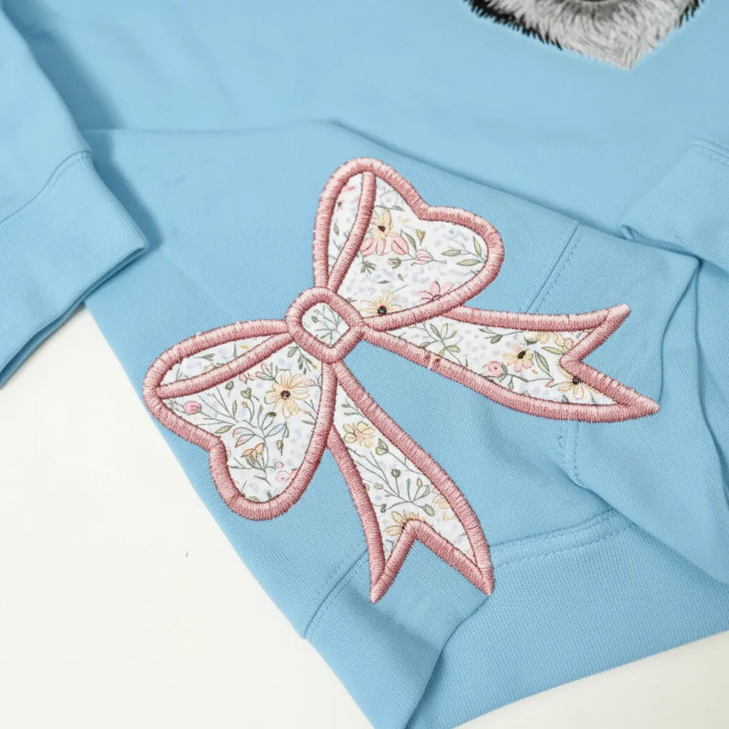 Close-up of a pink floral bow appliqué on a light blue sweatshirt
