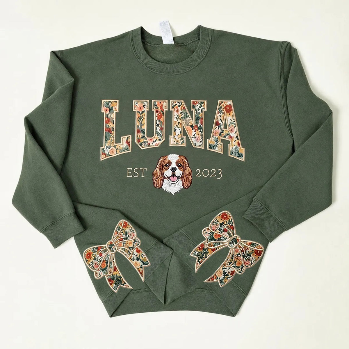 Forest green sweatshirt with LUNA in floral letters above an embroidered Cavalier spaniel and floral bows on the cuffs
