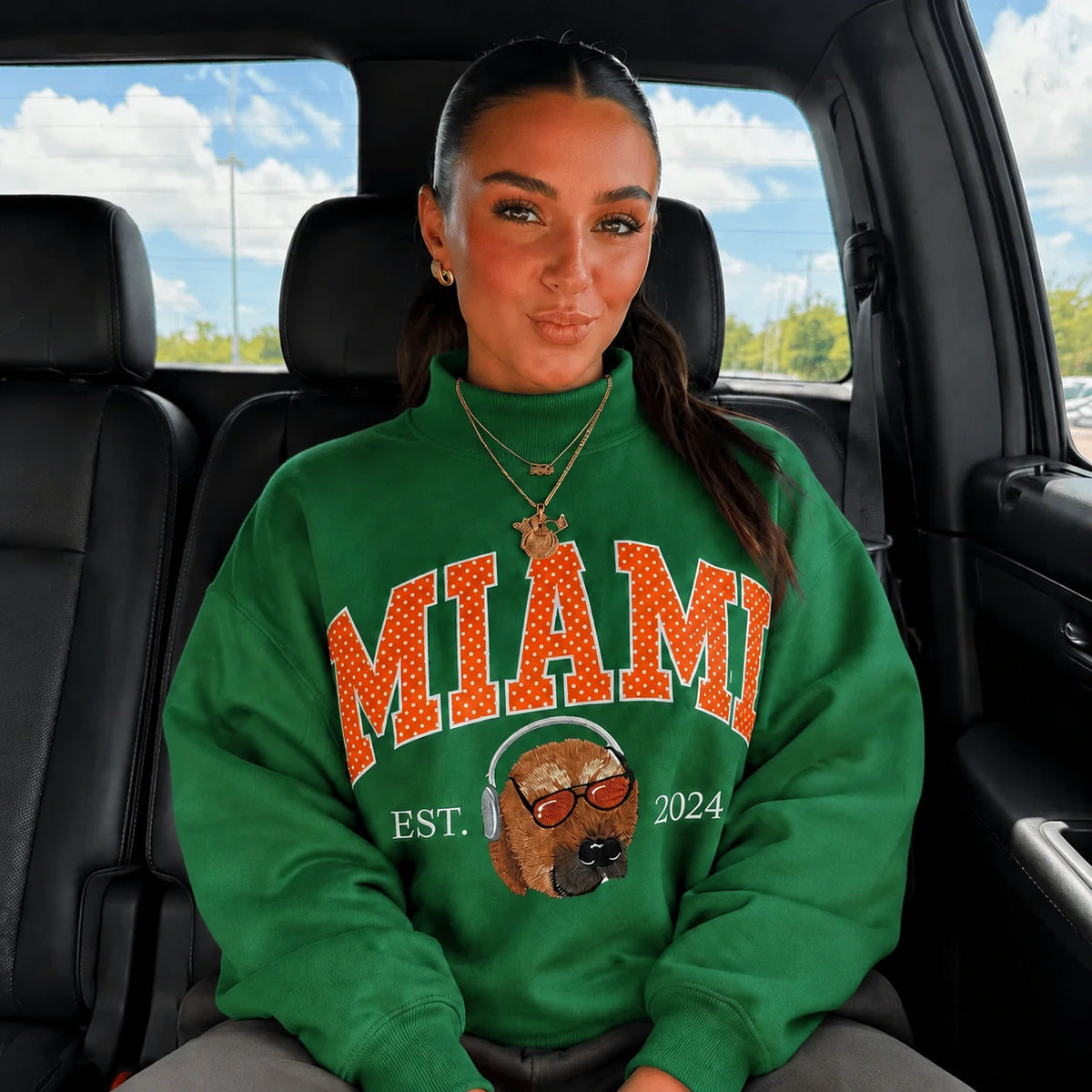 Woman in a green mockneck sweatshirt with MIAMI in orange polka-dot letters and an embroidered dog wearing headphones