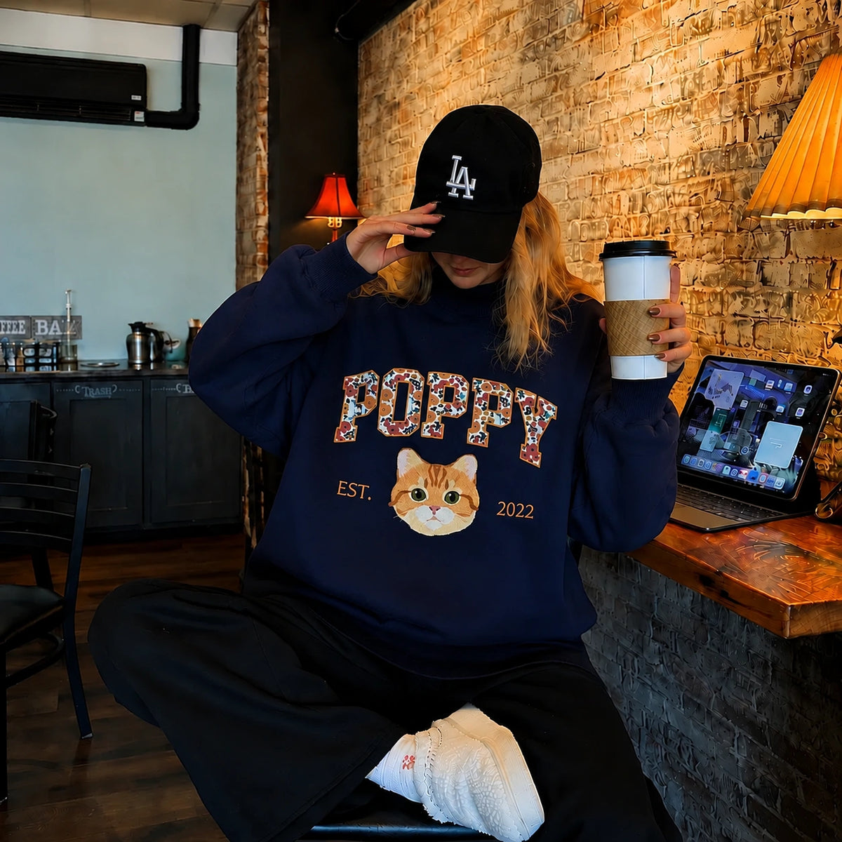 Woman in a navy mockneck sweatshirt with POPPY in floral letters above an embroidered orange cat