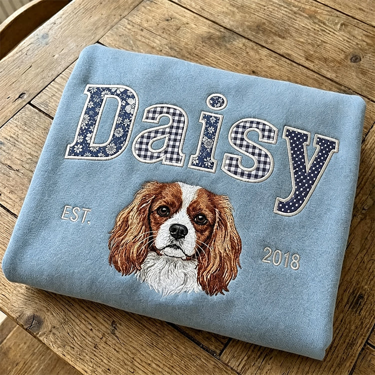Light blue sweatshirt with Daisy in navy patchwork fabric letters above an embroidered Cavalier King Charles spaniel