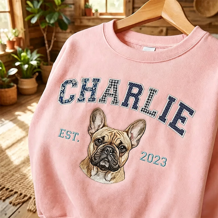 Pink sweatshirt with CHARLIE in navy patchwork letters above an embroidered French bulldog, on a hanger