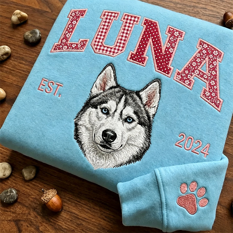 Light blue sweatshirt with LUNA in red patchwork letters above an embroidered husky, paw on the cuff
